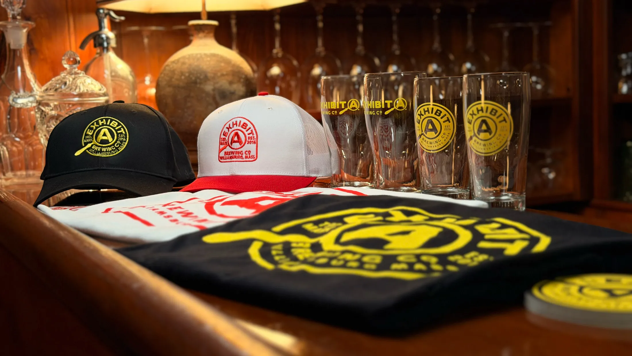 Close-up of Exhibit A merch displayed on the bar: hats, t-shirts, and branded glassware