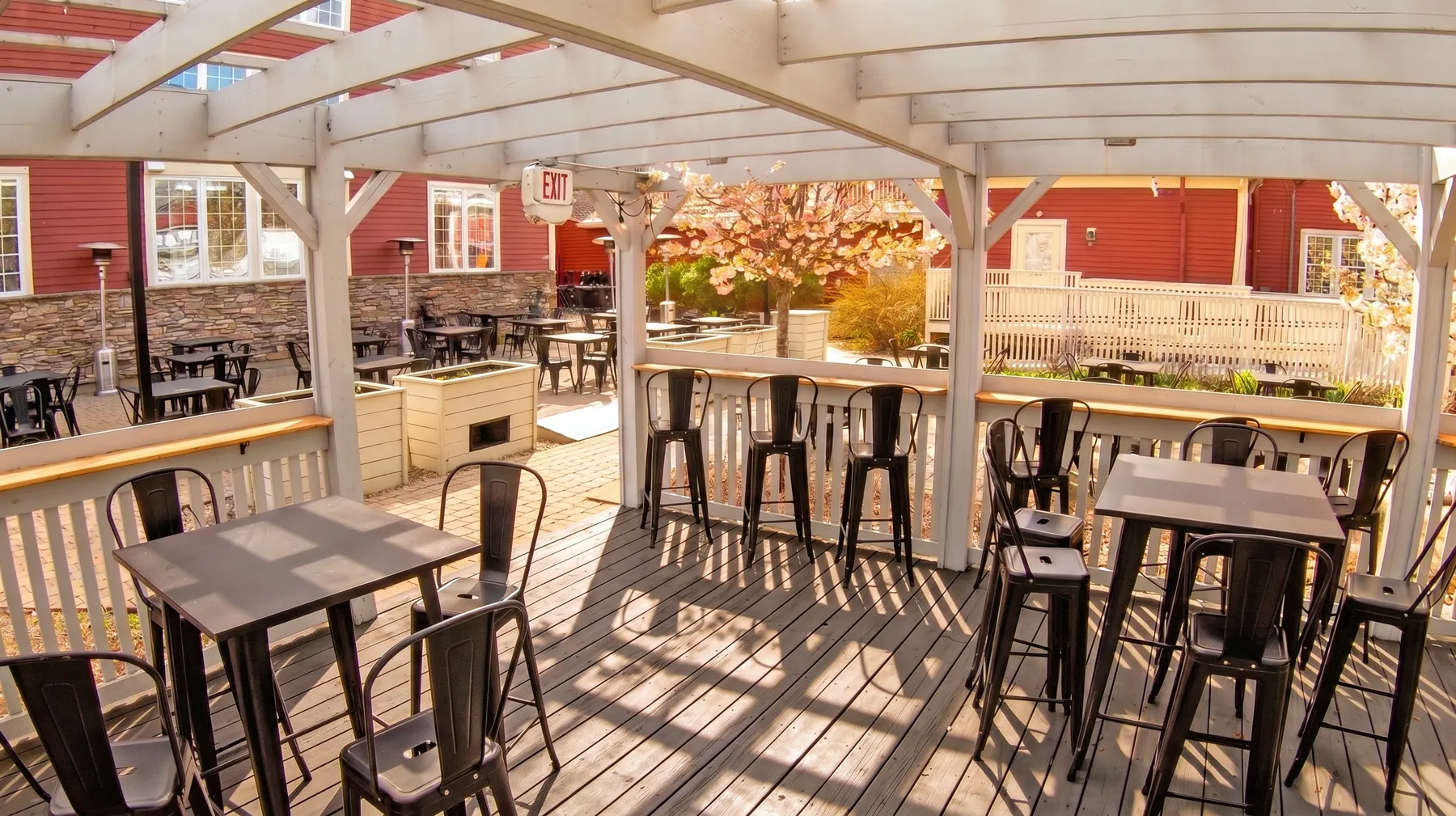 Sunny pergola-covered deck with bar tables and stools at Exhibit A