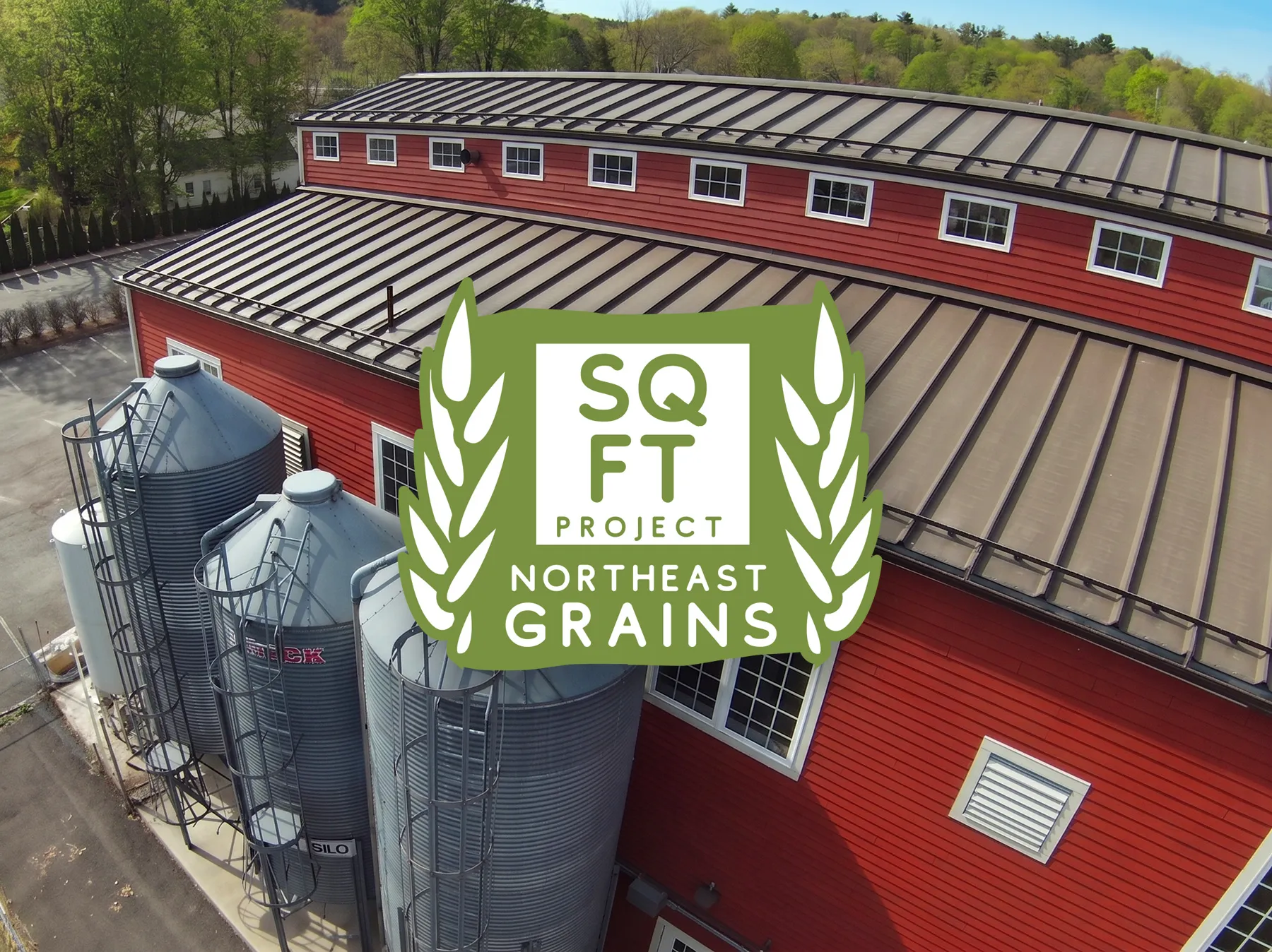 Aerial view of the Exhibit A Brewing red barn brewery and grain silos with the SQ FT Project Northeast Grains badge